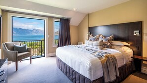 A bedroom with a large bed, a chair, a nightstand, and a view of the ocean through a balcony. - Platinum Queenstown Villas (Queenstown)