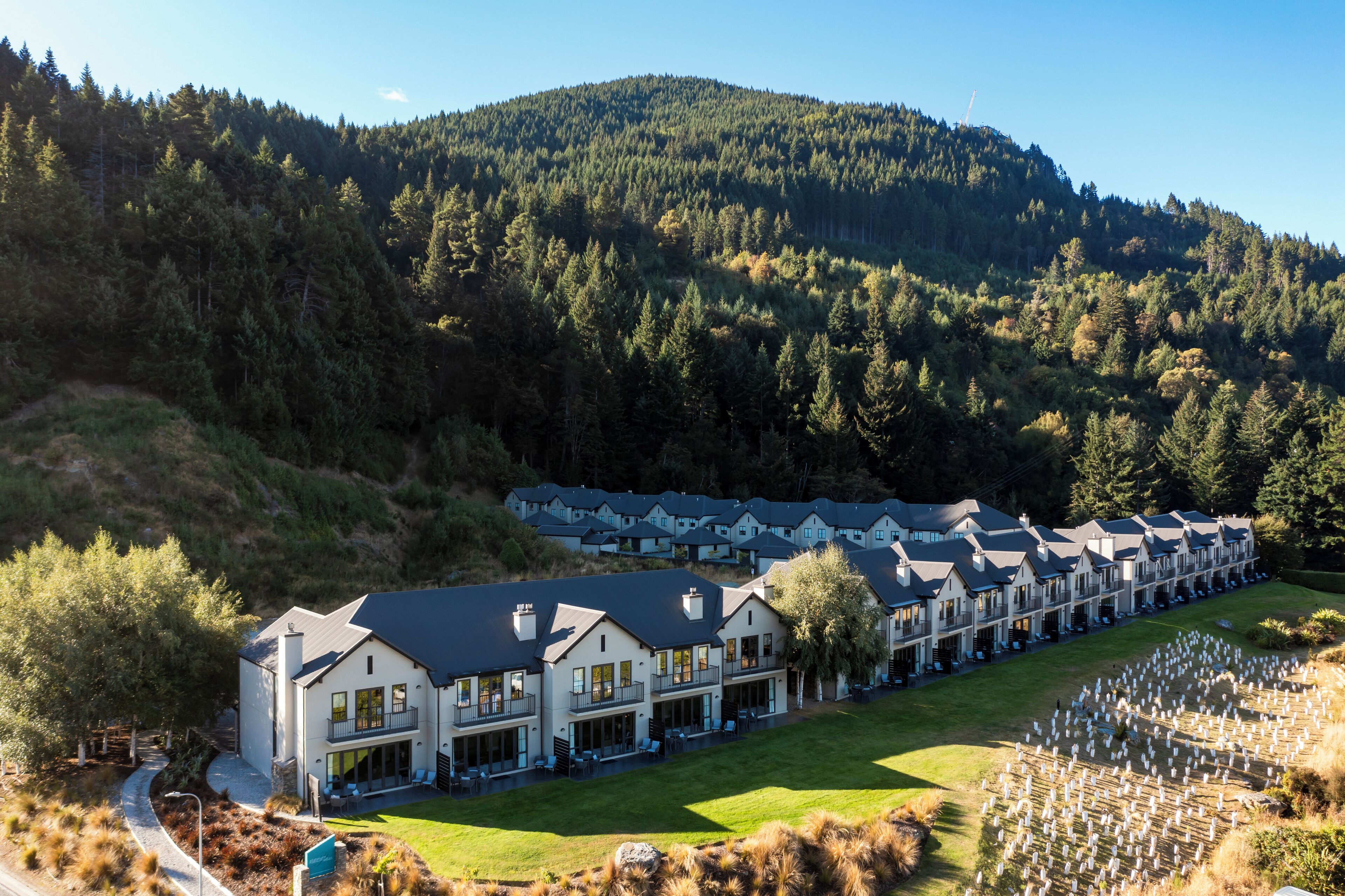 A large resort with multiple buildings, a well-maintained lawn, and a forested mountain backdrop.