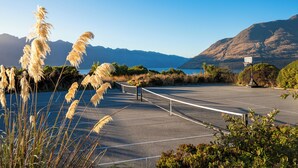 A tennis court with a net, surrounded by pampas grass and mountains in the background. - Platinum Queenstown Villas (Queenstown)