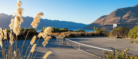 A tennis court with a net, surrounded by pampas grass and mountains in the background.