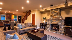 A modern living room with a stone fireplace, a sofa set, and a dining area with a staircase. - Platinum Queenstown Villas (Queenstown)