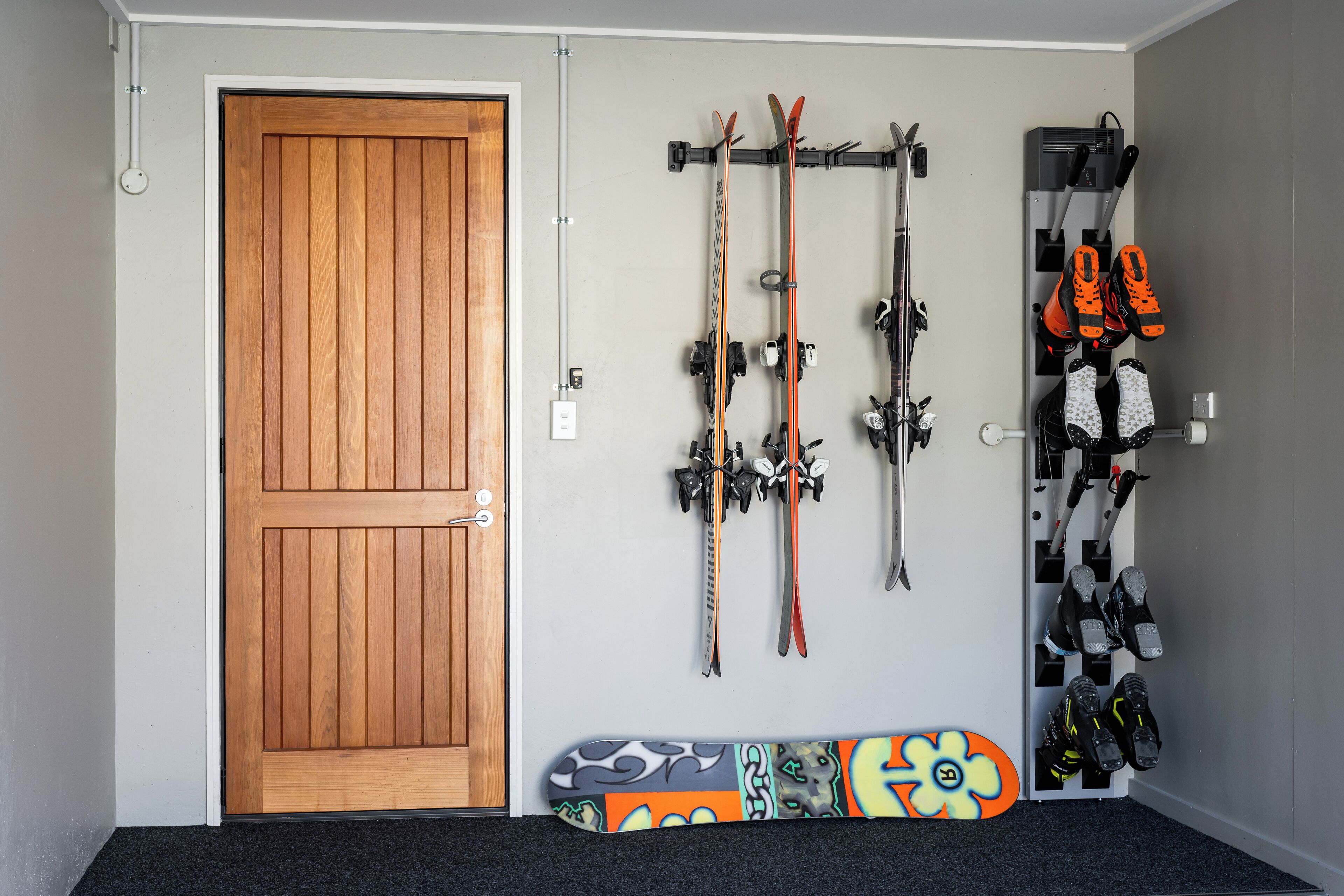 A room with a wooden door, skis, and ski boots on racks.
