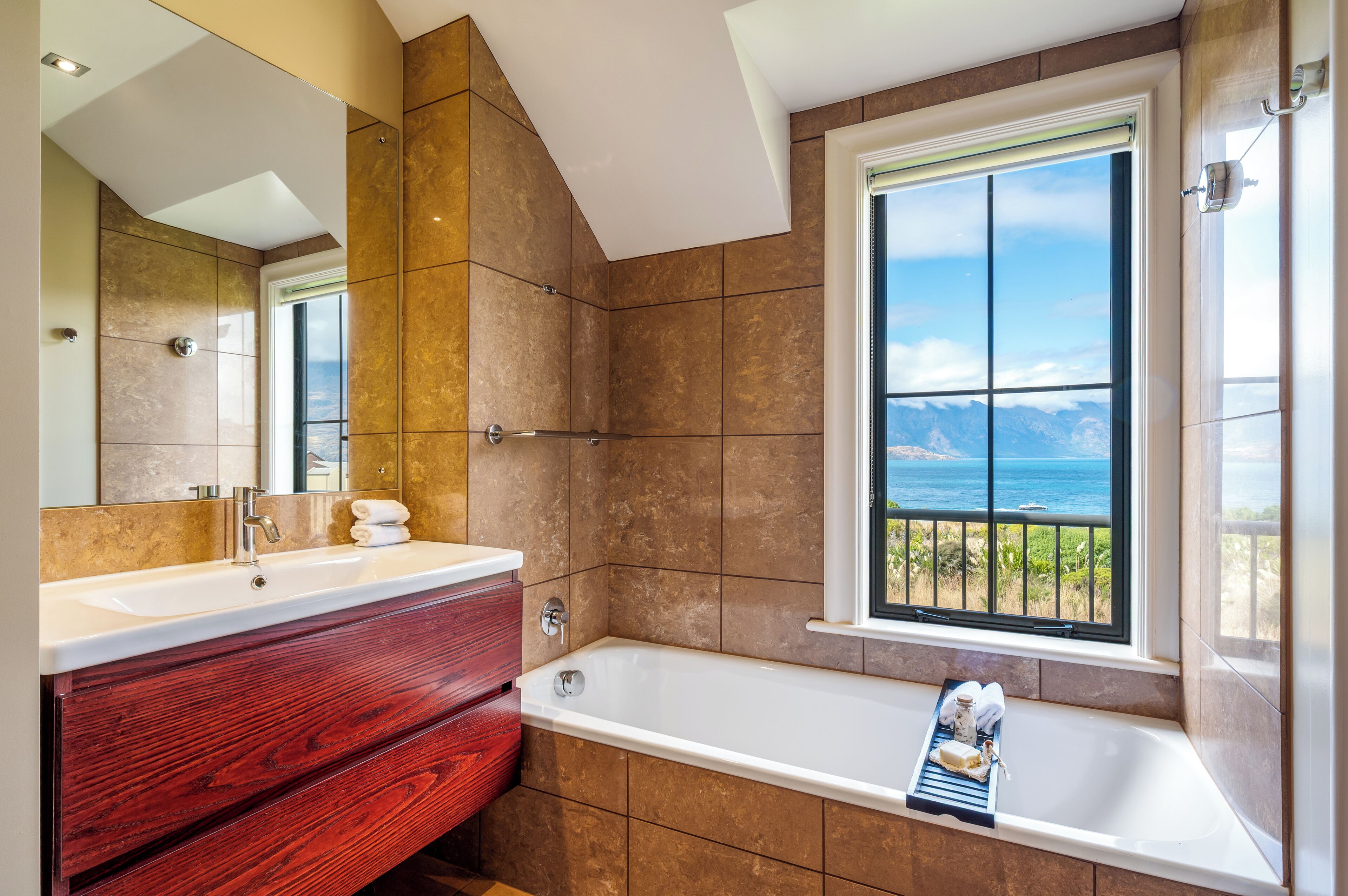 A bathroom with a large window, a bathtub, and a vanity with a mirror.