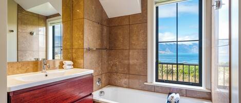 Une salle de bain dotée d’une grande fenêtre, d’une baignoire et d’un meuble-lavabo avec un miroir.