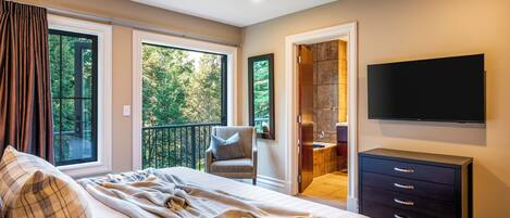 A bedroom with a large bed, a chair, a TV, and a view of the outdoors.