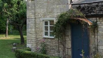 A stone building with a blue door, a small window, and a garden with grass and trees.