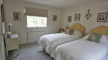 A bedroom with two beds, a window with a patterned curtain, a radiator, and framed pictures on the walls.