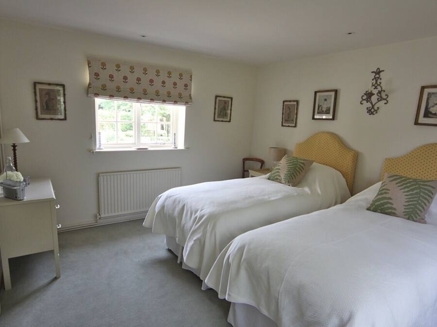A bedroom with two beds, a window with a patterned curtain, a radiator, and framed pictures on the walls.