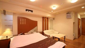 A hotel room with a large bed, a chair, a desk, and a lamp.