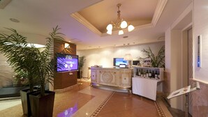 Et hotel lobby med en receptionsdisk, et fjernsyn og en lysekrone.