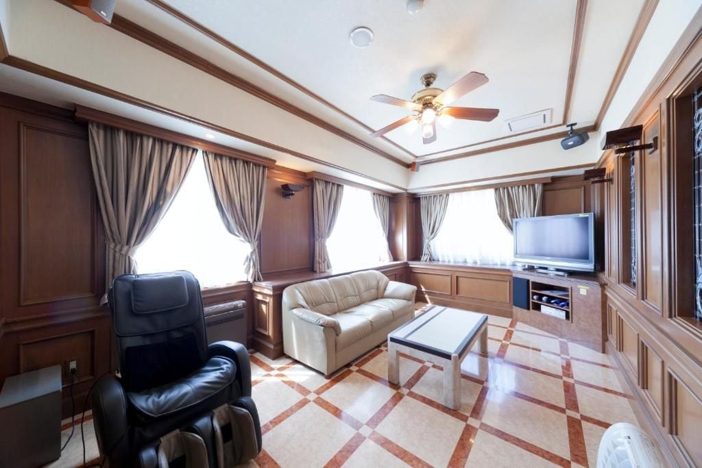Habitación de hotel con sofá de cuero, sillón reclinable, televisor de pantalla plana y ventilador de techo.