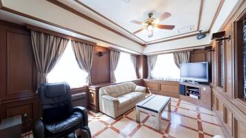 Habitación de hotel con sofá de cuero, sillón reclinable, televisor de pantalla plana y ventilador de techo.