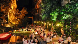 Una recepción de boda al aire libre con mesas y sillas redondas, frente a un imponente risco y exuberante vegetación.