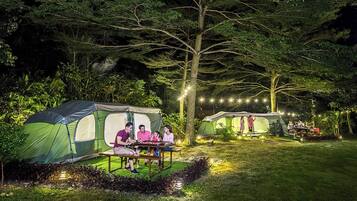 Een camping met tenten, een picknicktafel en lichtslingers.