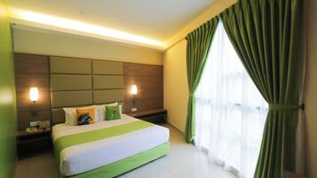 Quarto de hotel com uma cama grande, duas mesas de cabeceira, cabeceira com luminária e uma janela ampla com cortinas.