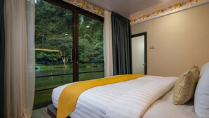 Habitación de hotel con una cama grande, vista a un bosque a través de una puerta corrediza de vidrio y un detalle amarillo en la colcha.