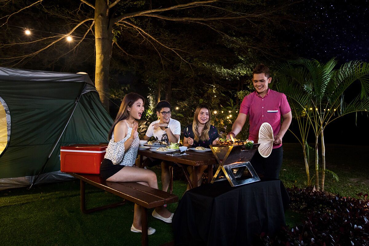 A group of people dining outdoors at night with a tent and a table set with food.
