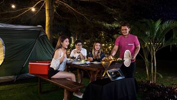 A group of people dining outdoors at night with a tent and a table set with food.