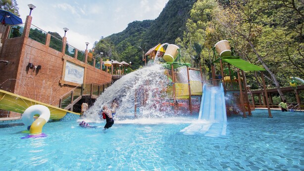 Parque acuático con piscina, toboganes y montañas al fondo.
