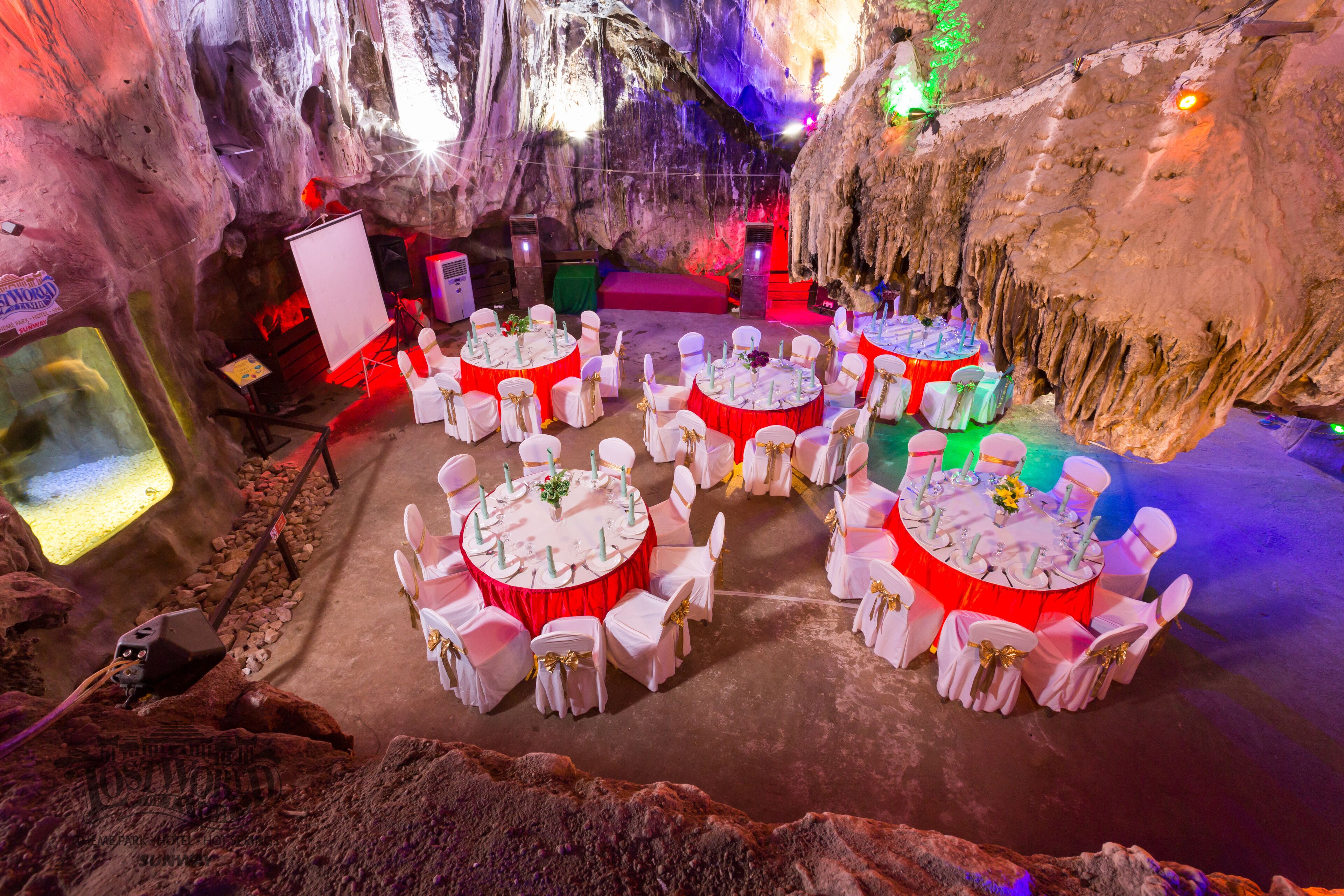 A cavernous venue with round tables and chairs, illuminated by ambient lighting, set against a backdrop of natural rock formations.