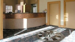 A hotel reception area with a curved counter, a telephone, and a reception desk. There are two doors and a patterned floor design. - Tropicana Suite Hotel (Vancouver)