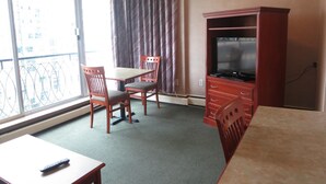 A hotel room with a balcony, a dining table with chairs, a TV cabinet, and a remote control on the table. - Tropicana Suite Hotel (Vancouver)