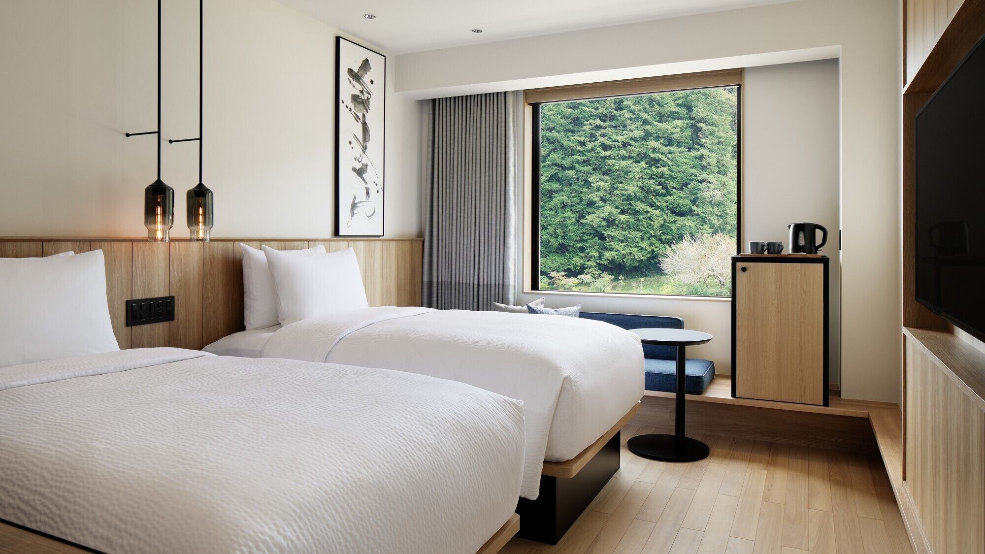A hotel room with two beds, a large window with a forest view, a small table, and a TV.
