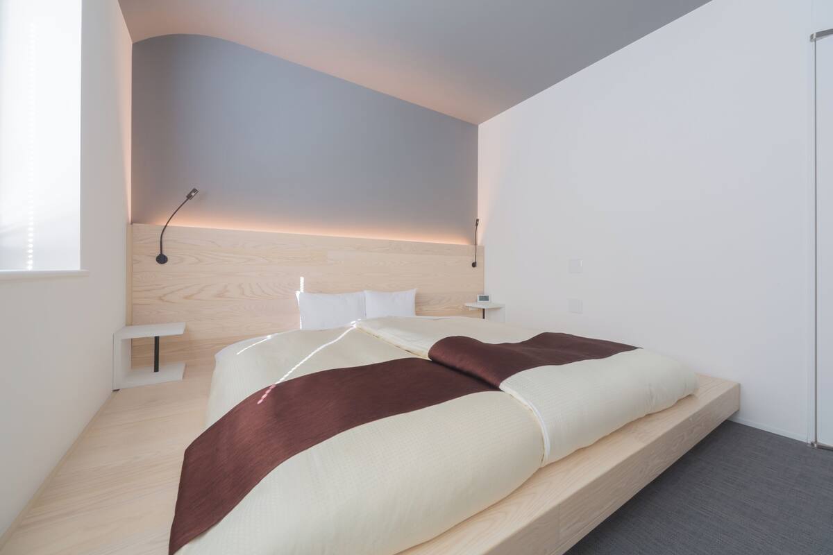 Un dormitorio moderno con cabecera de madera, una mesita de noche y una cama grande con manta marrón.
