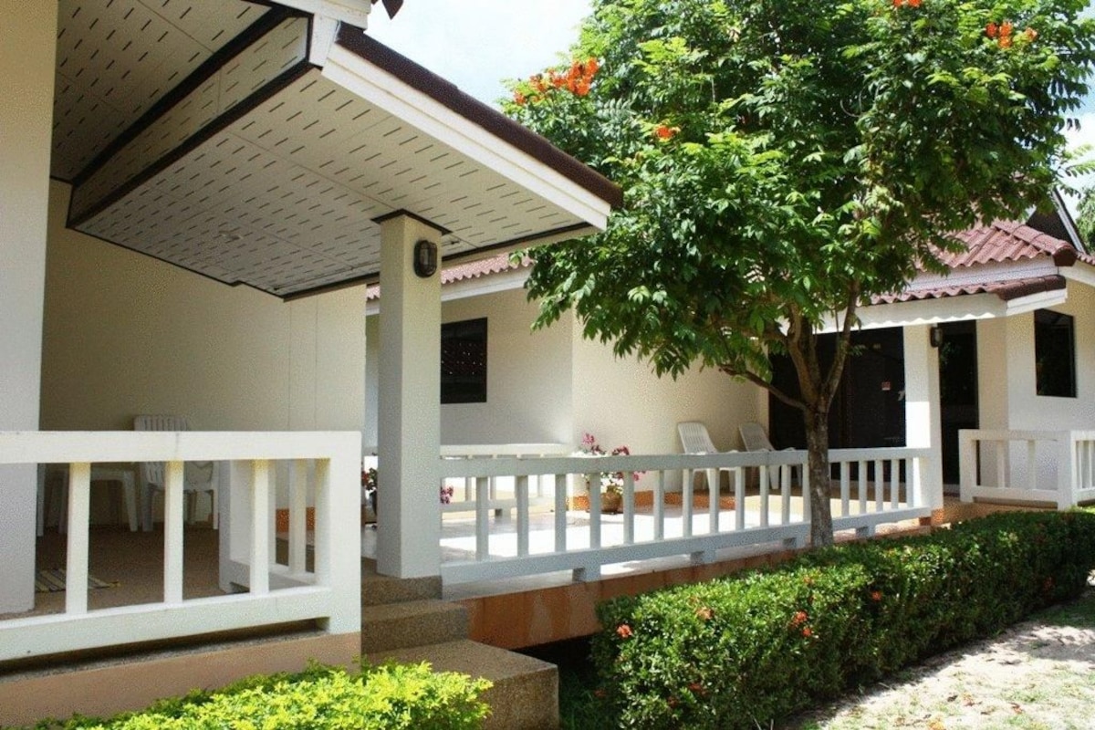 A two-story building with a covered porch, white railings, and a tree with orange flowers.