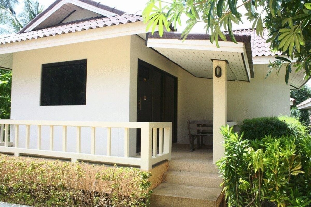 A single-story building with a porch, a small table, and a chair.