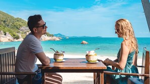 A couple seated at a wooden table with a view of a beach and ocean. - Promtsuk Buri Resort (Koh Samui)