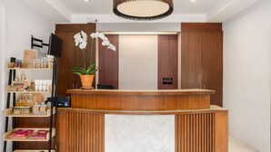 A reception area with a wooden reception desk, a potted orchid, and a shelf with various items. - Promtsuk Buri Resort (Koh Samui)