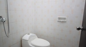 A small, clean bathroom with a toilet, a shower, and a small shelf. - Bakung Sunset Hotel (Kuta)
