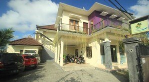 A two-story residential building with a balcony, parked cars, and motorcycles in front. - Bakung Sunset Hotel (Kuta)
