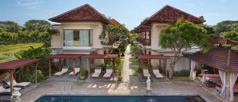 A pool area with two buildings, each with a tiled roof and a covered seating area.