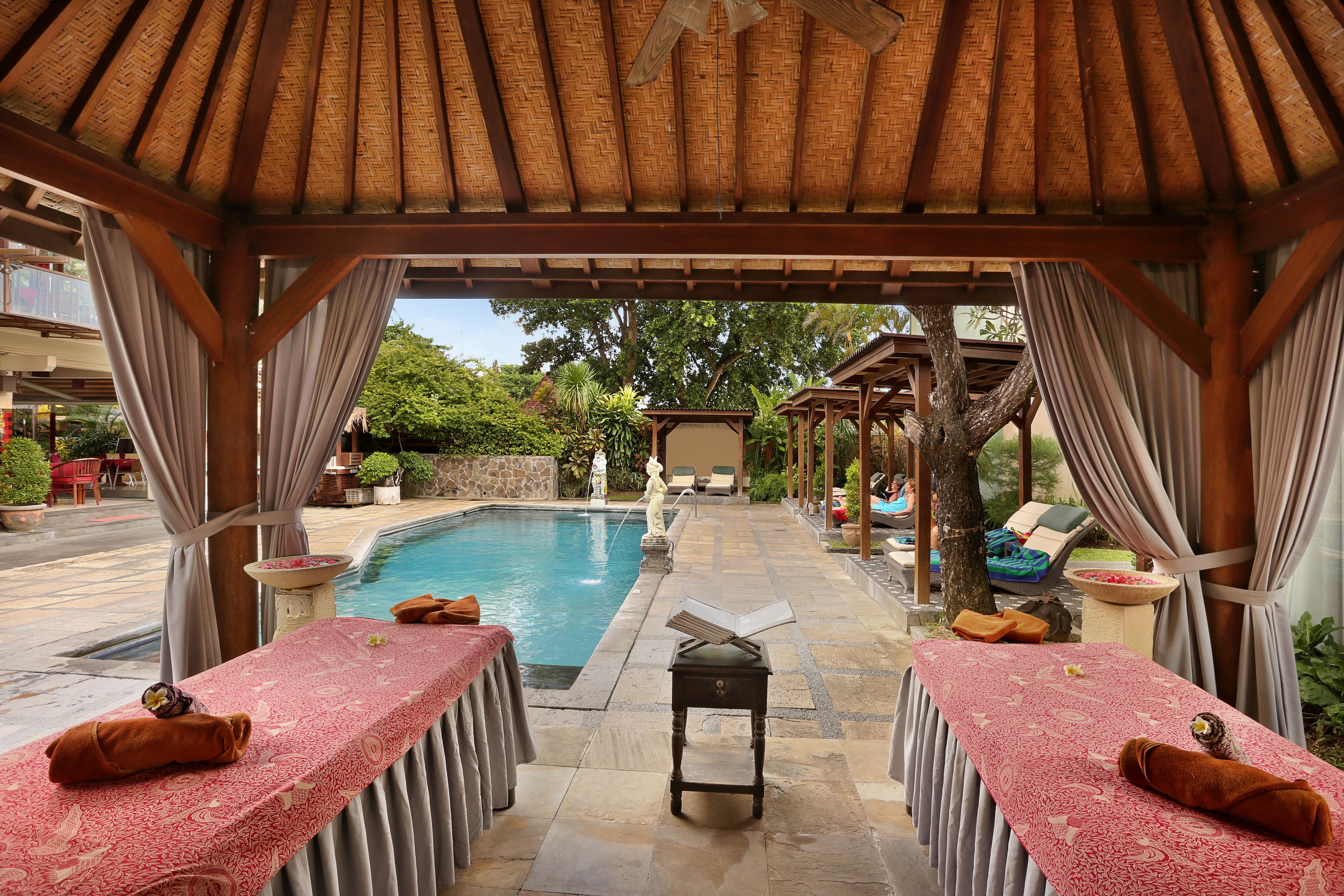 A poolside area with two massage tables, a small table with a book, and a statue.