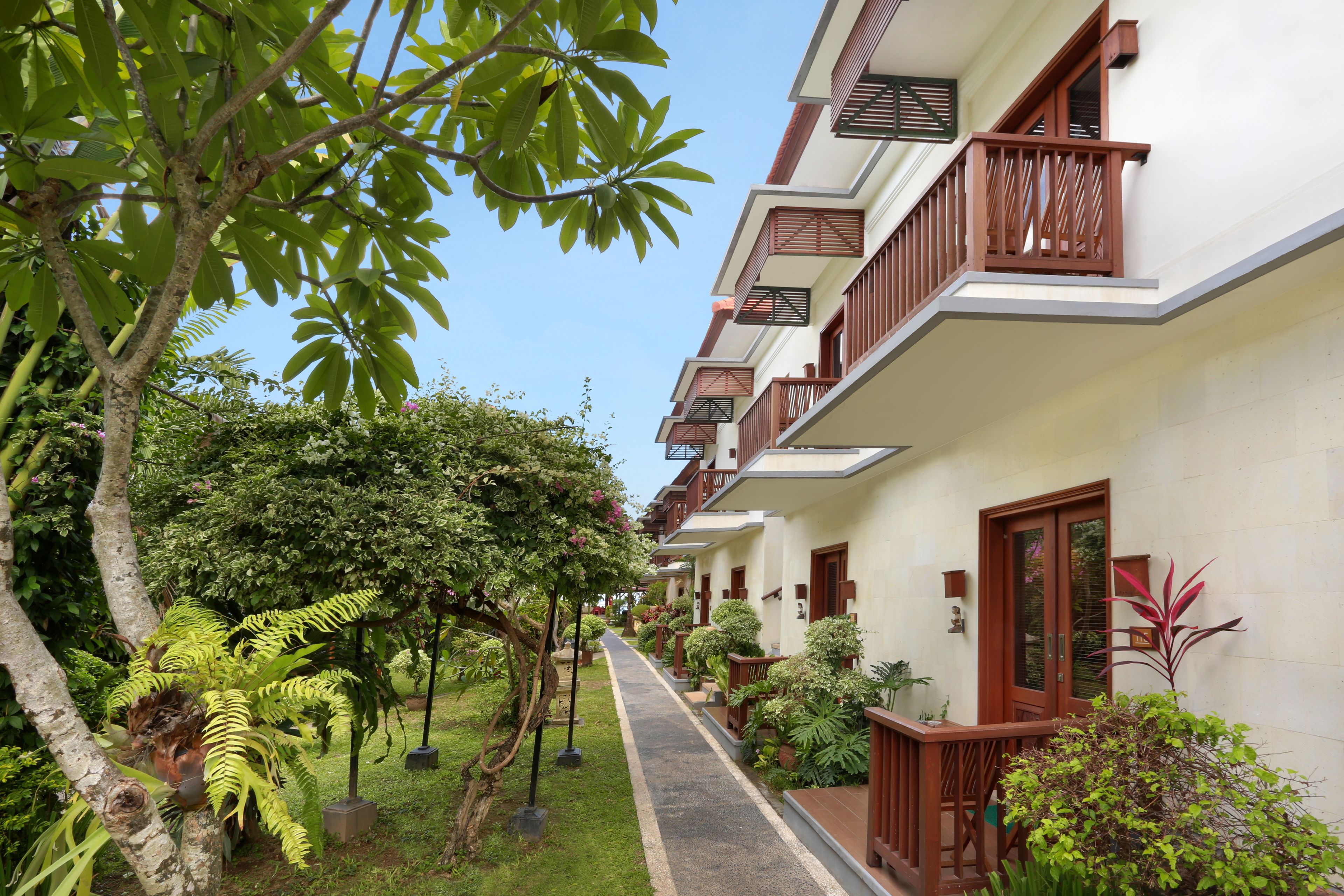 A row of white buildings with wooden balconies and a pathway lined with greenery.