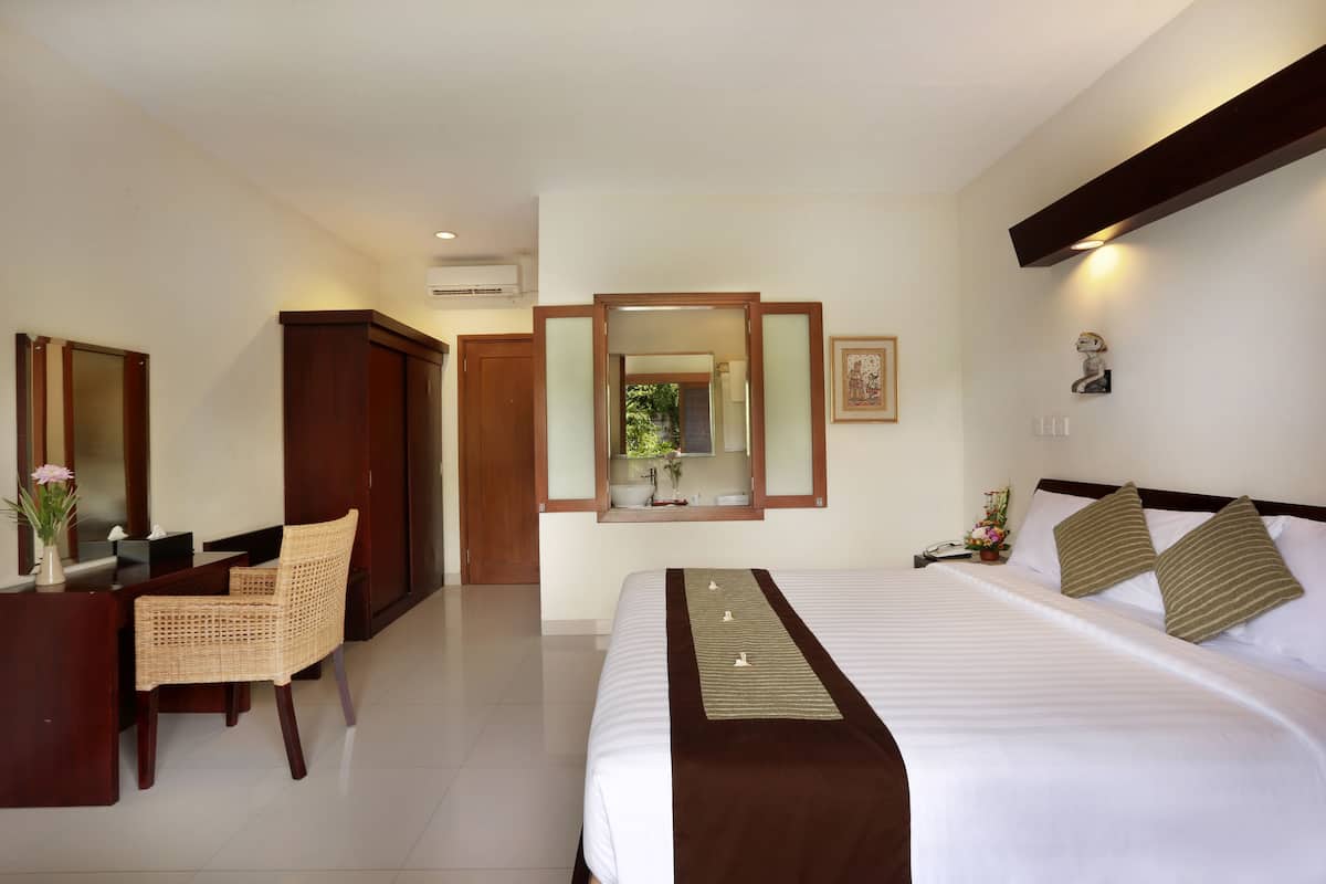 Une chambre d’hôtel avec un grand lit, un bureau avec une chaise, un miroir et une petite fenêtre.