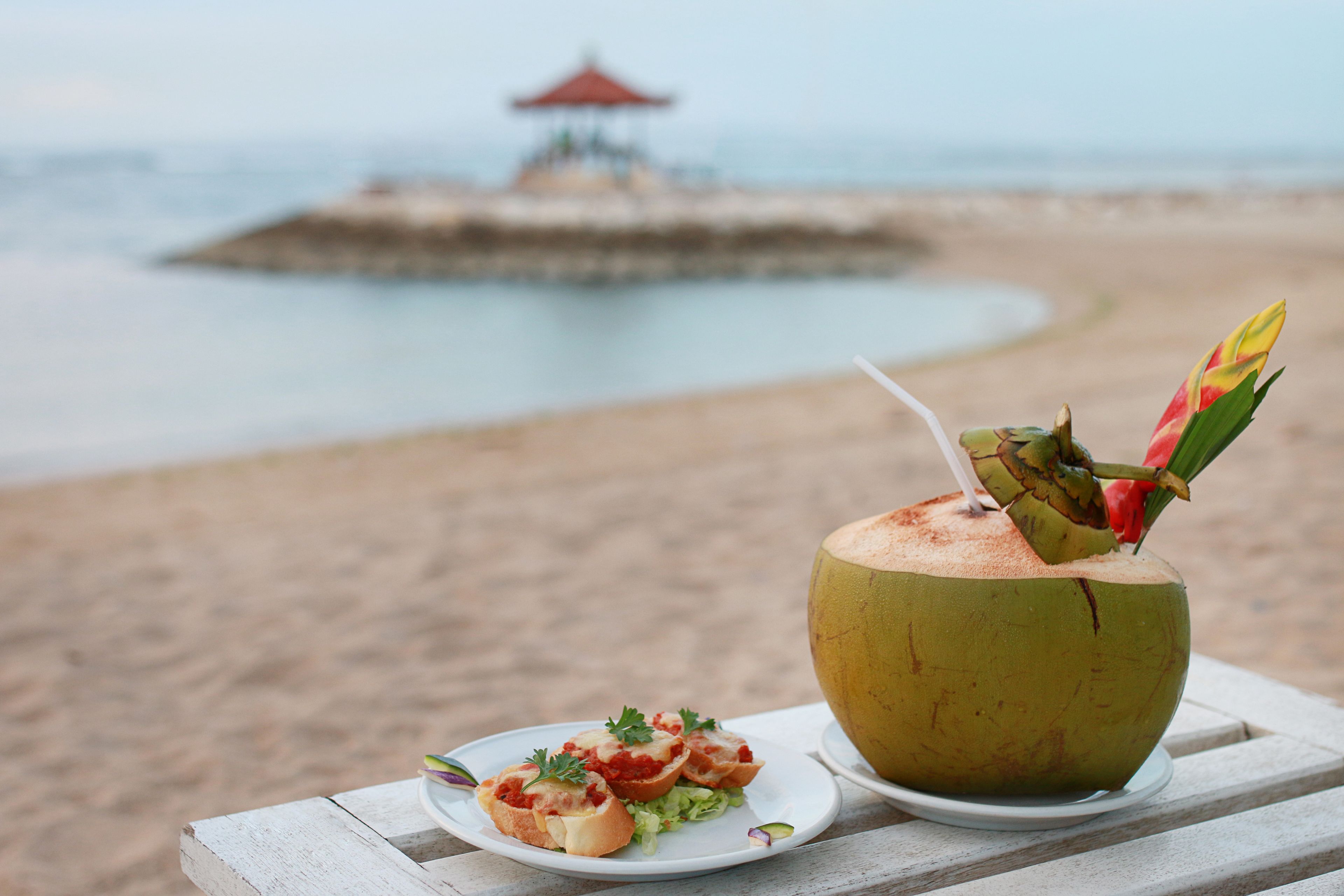 A beachside table with a coconut drink and a plate of food.