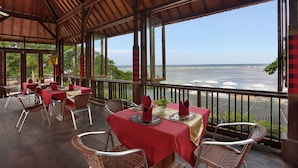 Un espacio de comedor al aire libre con mesas dispuestas para dos personas, con vista al océano.