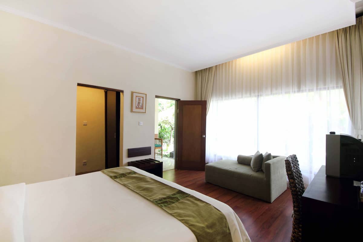 Une chambre d’hôtel avec un lit, un canapé, une télévision et une fenêtre avec des rideaux.