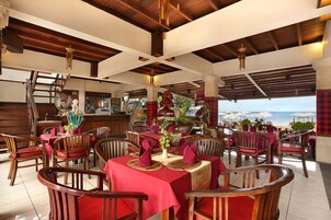 A restaurant with wooden furniture, red tablecloths, and a view of the sea.