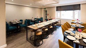 A conference room with long tables, chairs, and a window with blinds. - Garden Court Hotel (London)