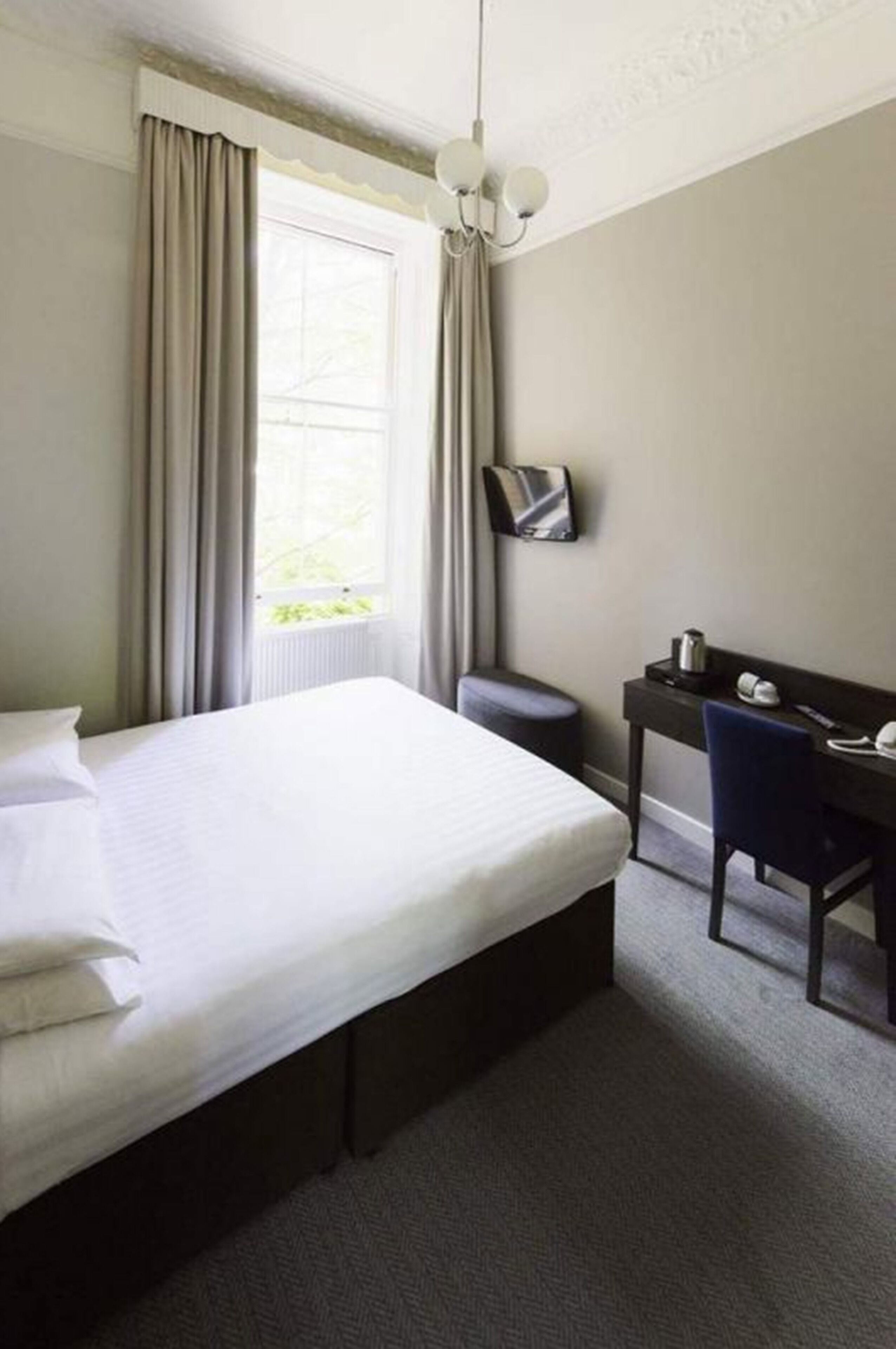 A hotel room with a large bed, a desk with a chair, a flat-screen TV, and a window with curtains.
