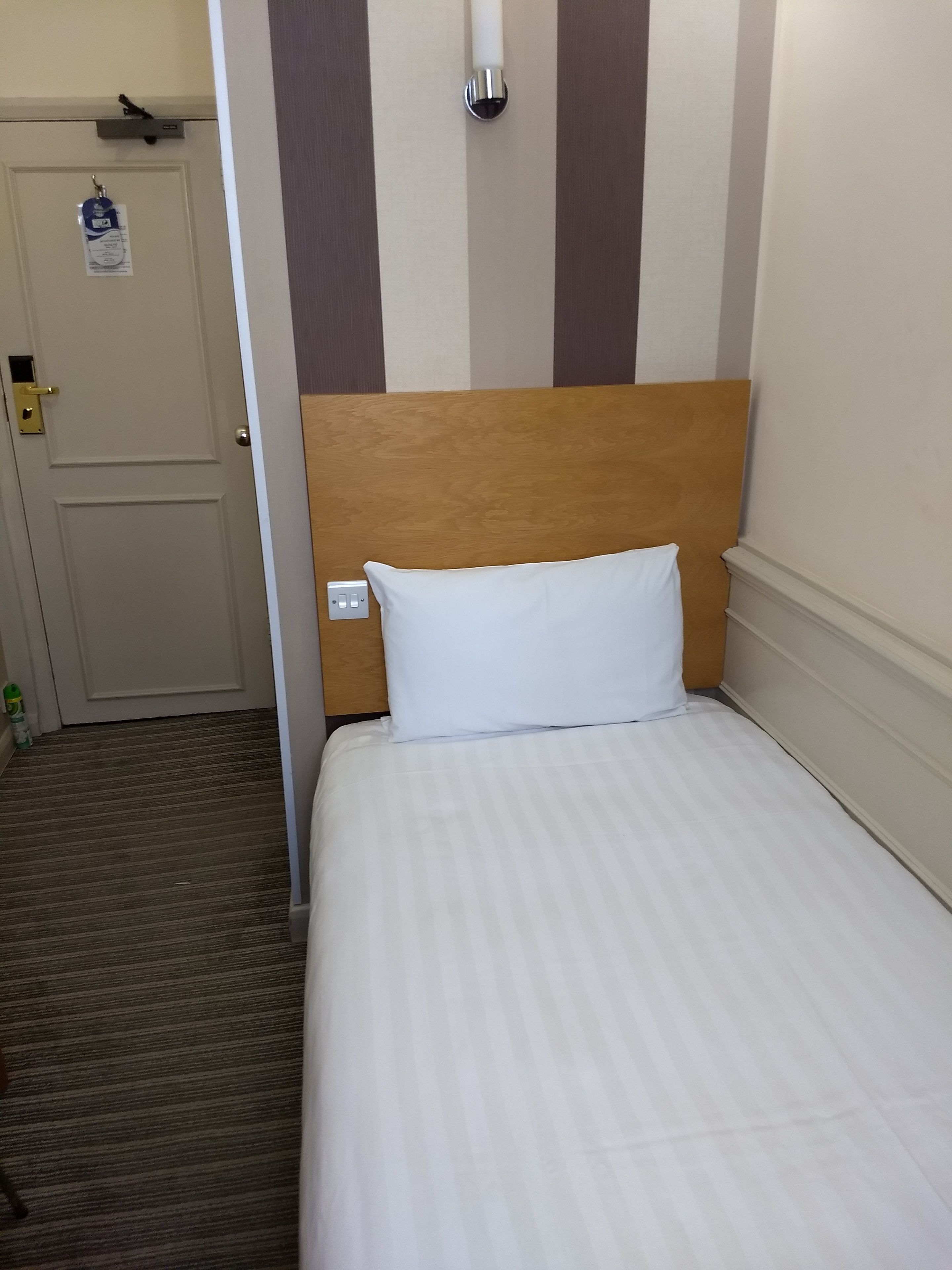 A hotel room with a wooden headboard, a white pillow, and a door with a keycard lock.