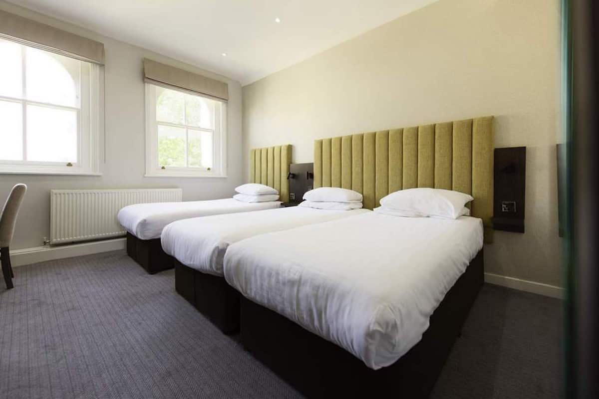 Et hotelværelse med to senge, en radiator, et vindue og en stol.