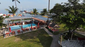 A pool area with lounge chairs and umbrellas, a covered seating area, and a view of boats on the water. - Kids Heaven Villa (Koh Samui)
