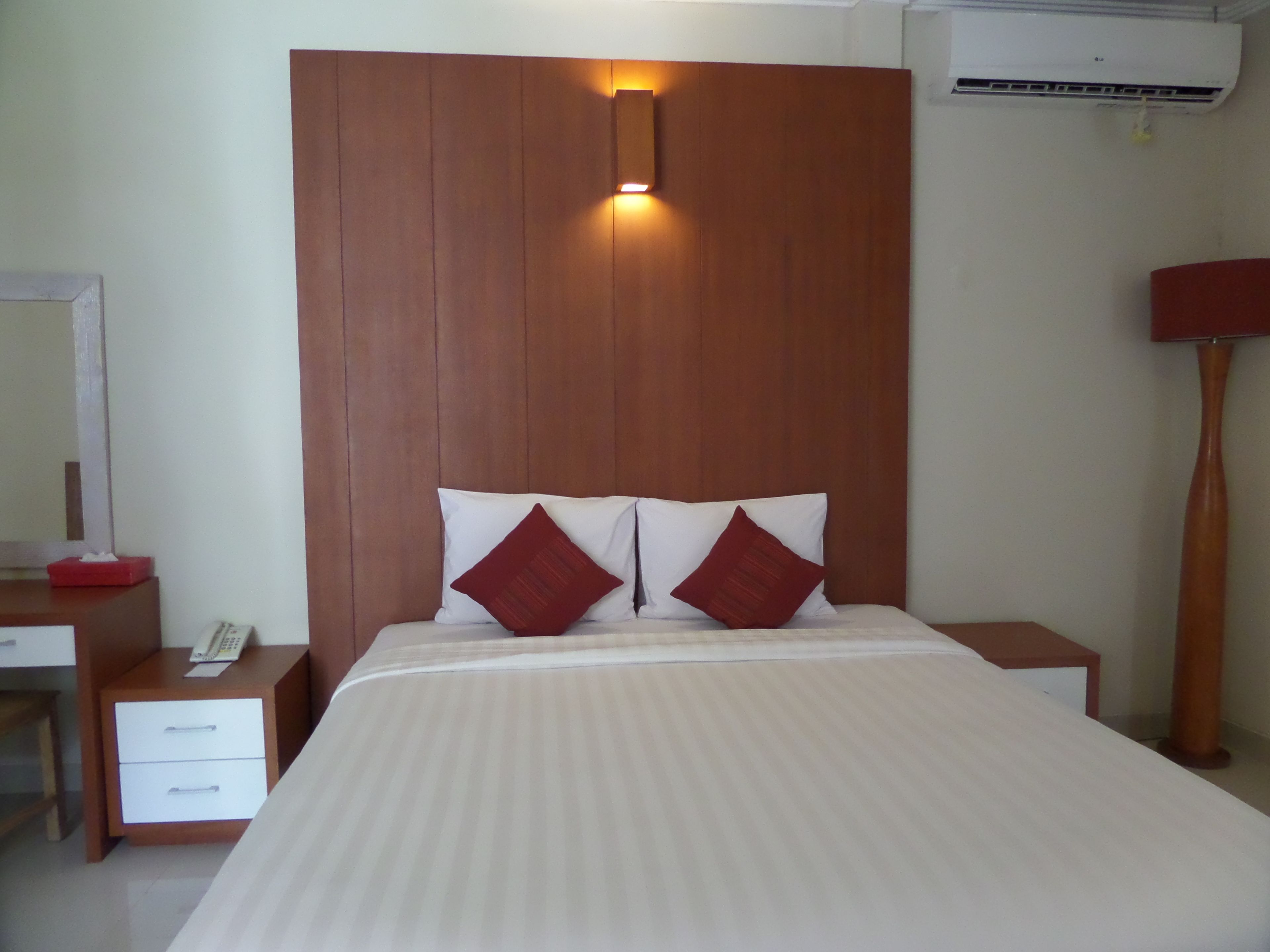 Habitación de hotel con cabecera de madera, mesita de noche con lámpara, teléfono y una pequeña caja roja.