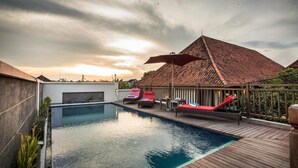 A swimming pool with lounge chairs and a covered area with a tiled roof. - Svarna Hotel Sanur (Denpasar)