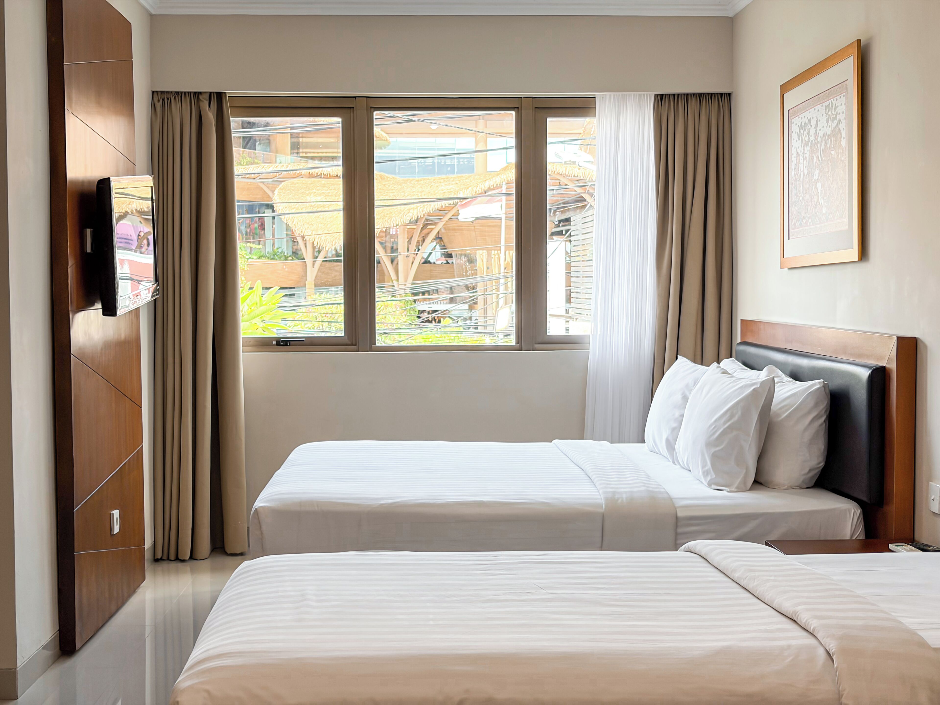 Una habitación de hotel con dos camas, un televisor montado en la pared y una ventana con cortinas.
